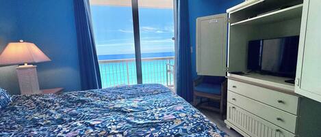 A room with a bed, a television, a dresser, and a view of the ocean.
