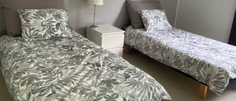 A bedroom with two beds, a nightstand, a lamp, and a wall painting.