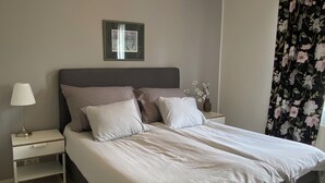 Ein Schlafzimmer mit einem Bett, Nachttischen, einer Lampe, einem gerahmten Bild, einem blumigen Vorhang und einer Deckenleuchte.