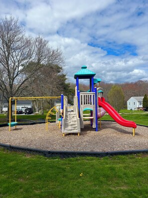 Ein Spielplatz mit Rutsche, Kletterbereich und einem überdachten Spielhäuschen.