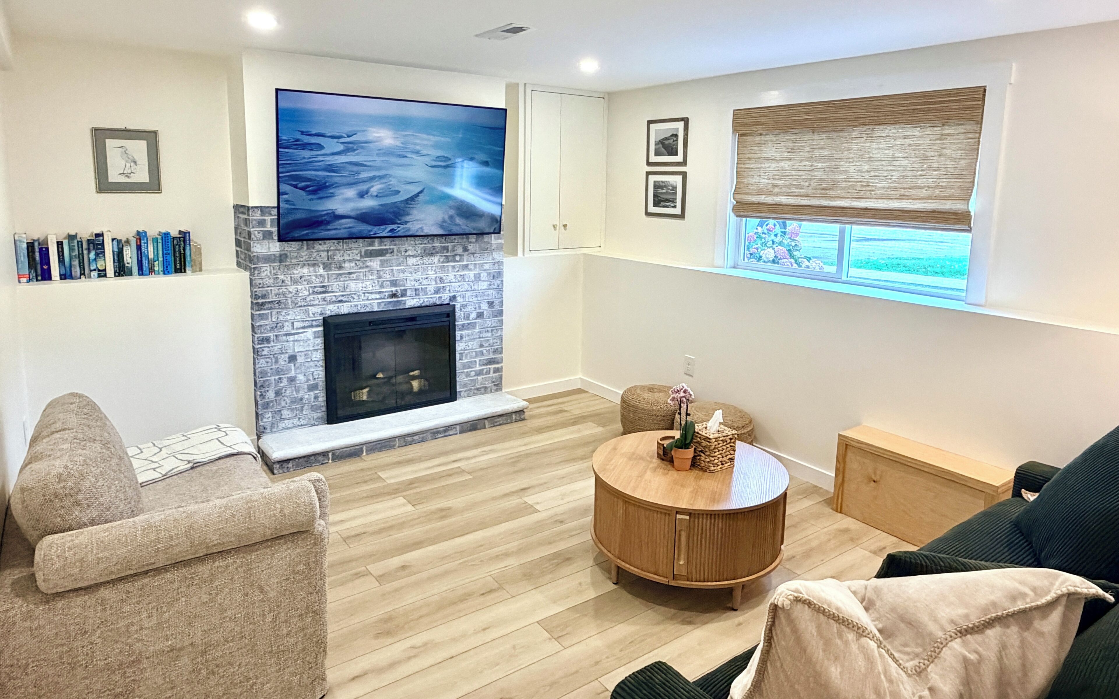 A living room with a fireplace, a flat-screen TV, a round wooden coffee table, and a window with blinds.