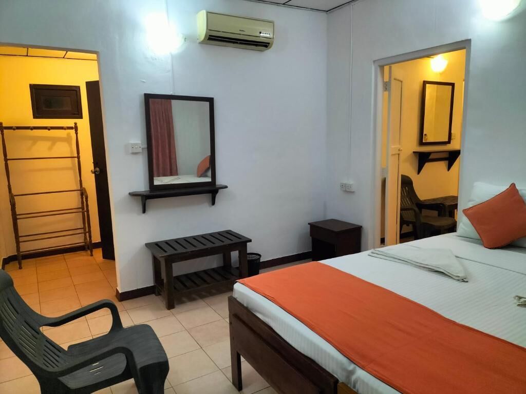 A bedroom with a bed, a desk, a chair, a mirror, and an air conditioning unit.