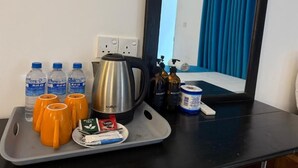 A tray with toiletries, a kettle, and a mirror reflecting a room with a blue curtain.