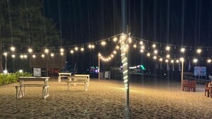 A beach setting with string lights, a bench, and a sign.