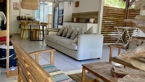 Una terraza de madera con un sofá, un banco, una zona de comedor y una cocina al fondo.