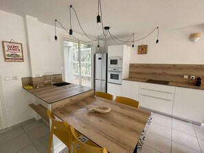 A modern kitchen with a wooden dining table, yellow chairs, a built-in oven, and a refrigerator.