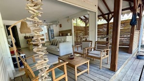 Una terraza de madera con un sofá y sillas, una planta colgante y una cocina al fondo.