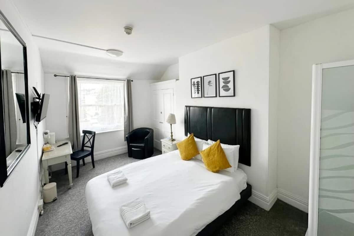 A hotel room with a bed, a desk, a chair, a mirror, and a window.