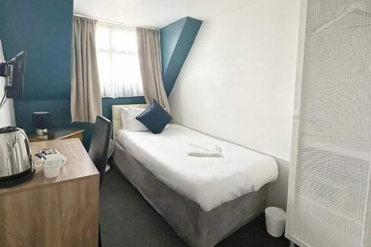 A hotel room with a bed, desk, chair, and a window with curtains.