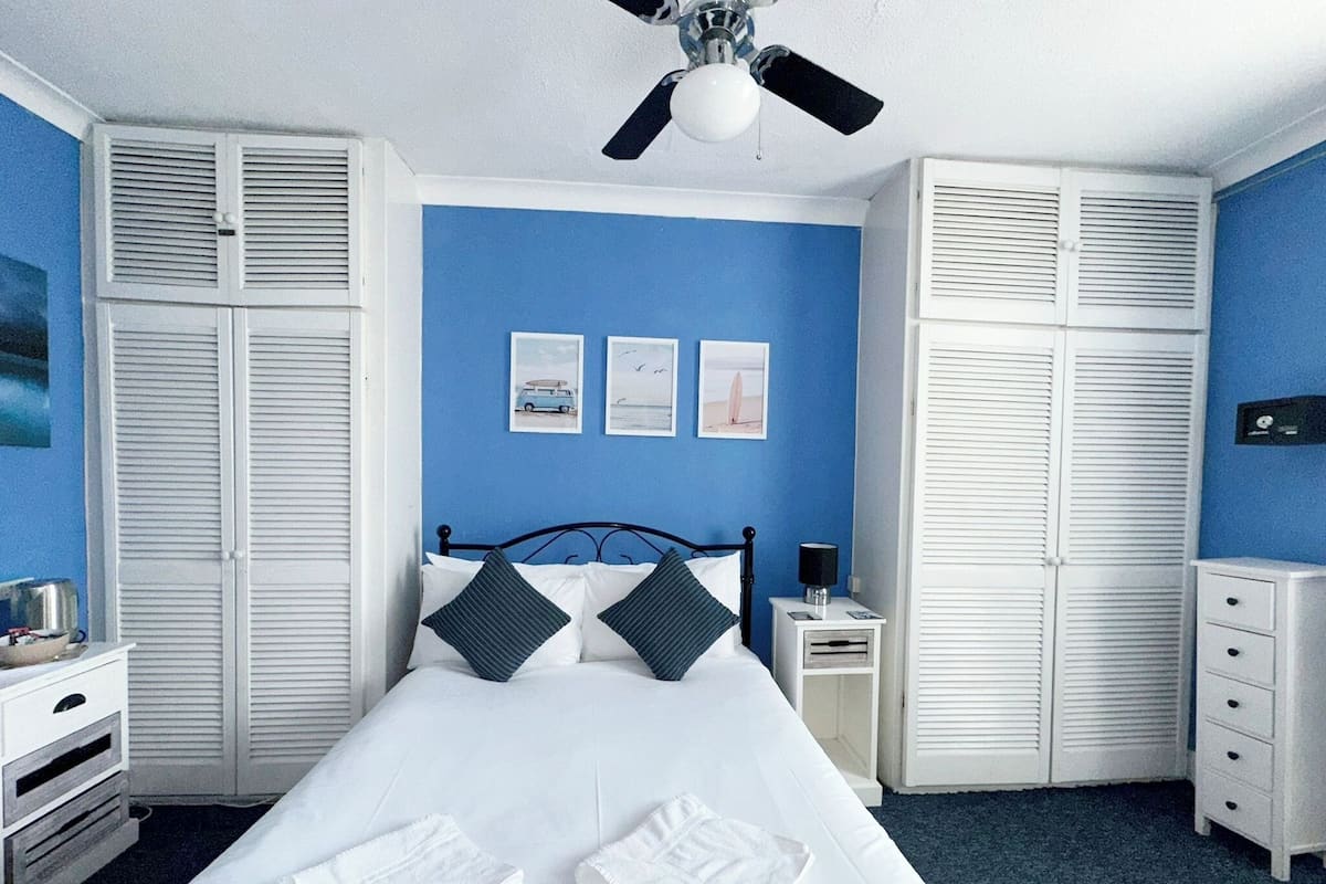 A bedroom with a bed, white nightstands, a ceiling fan, and a wardrobe.