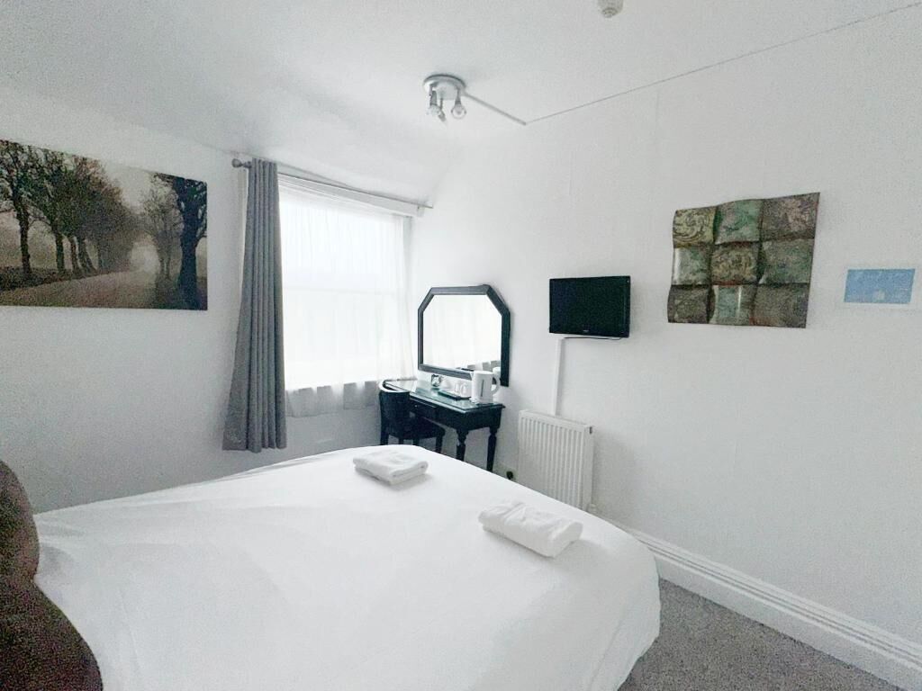 A hotel room with a bed, a desk, a mirror, a television, and artwork on the walls.