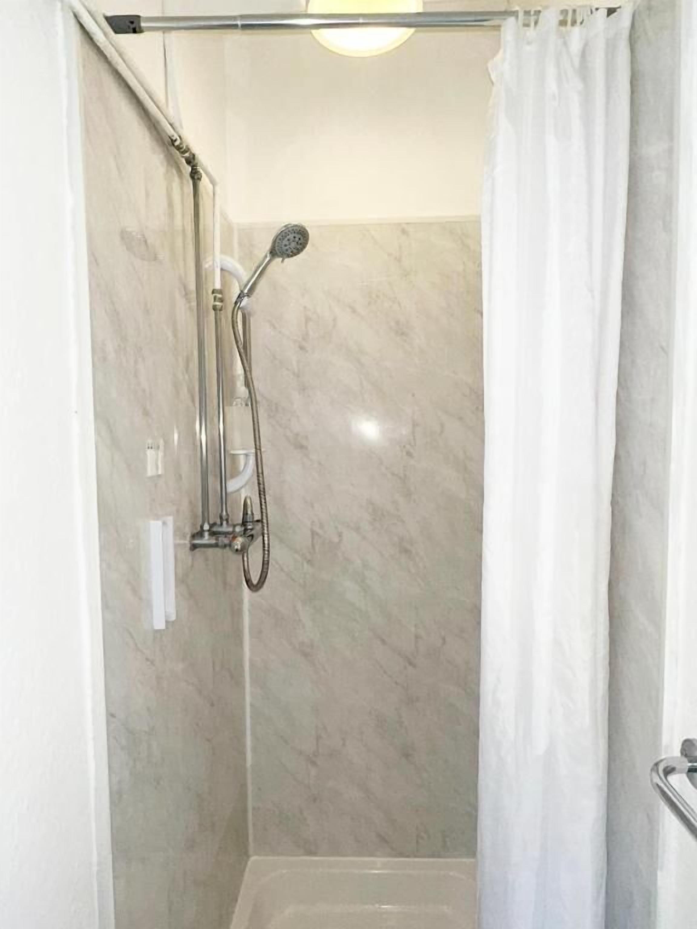 A shower with a handheld showerhead, a wall-mounted faucet, and a glass door.