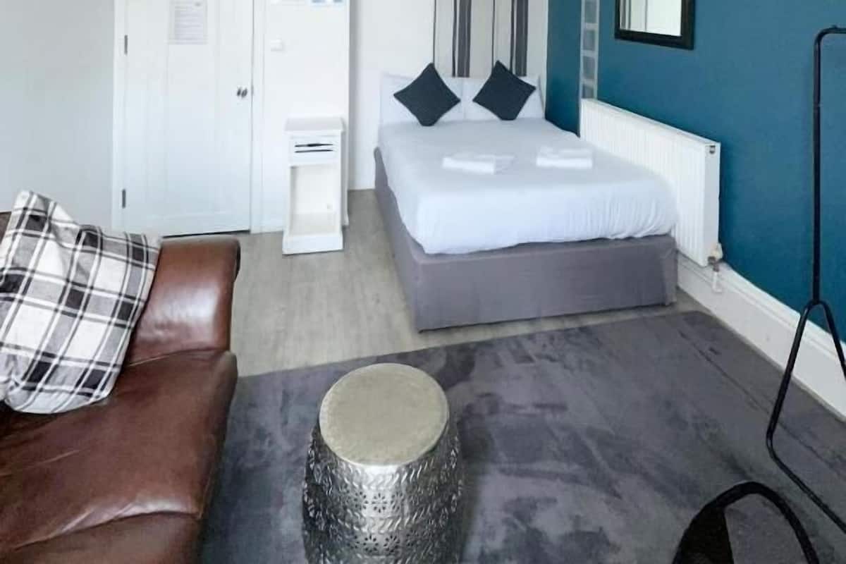 A bedroom with a bed, a white wardrobe, a brown leather sofa, a small round table, and a blue accent wall.