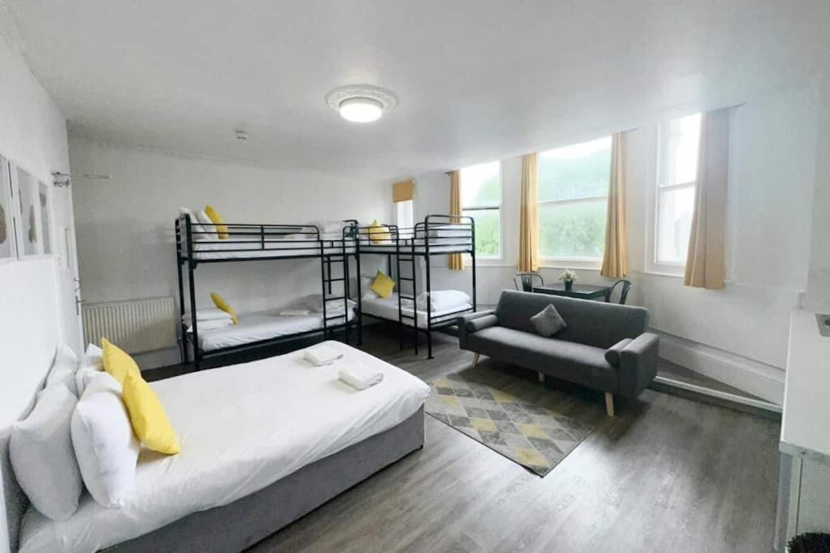 A dormitory room with bunk beds, a sofa, a table, and a window.