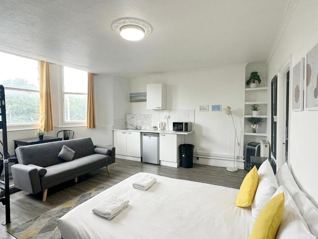 Een moderne hotelkamer met een bed, een bank, een kitchenette en uitzicht op de omgeving.