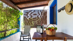 A patio with a table, chairs, a bottle of wine, and a basket of fruit.