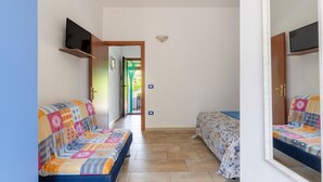 A room with a sofa, a bed, a TV mounted on the wall, and a door leading to another room.