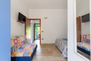 Una habitació amb un sofà, un llit, un televisor fixat a la paret i una porta que dóna a una altra estança.