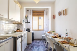 Une cuisine de taille réduite avec un coin repas, une fenêtre avec des rideaux et un sol carrelé.