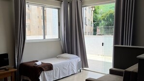Habitación de hotel con cama, sofá, televisión y balcón con cortinas.