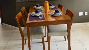 Un comedor con una mesa de madera dispuesta para cuatro personas, sillas y una cocina a la vista al fondo.