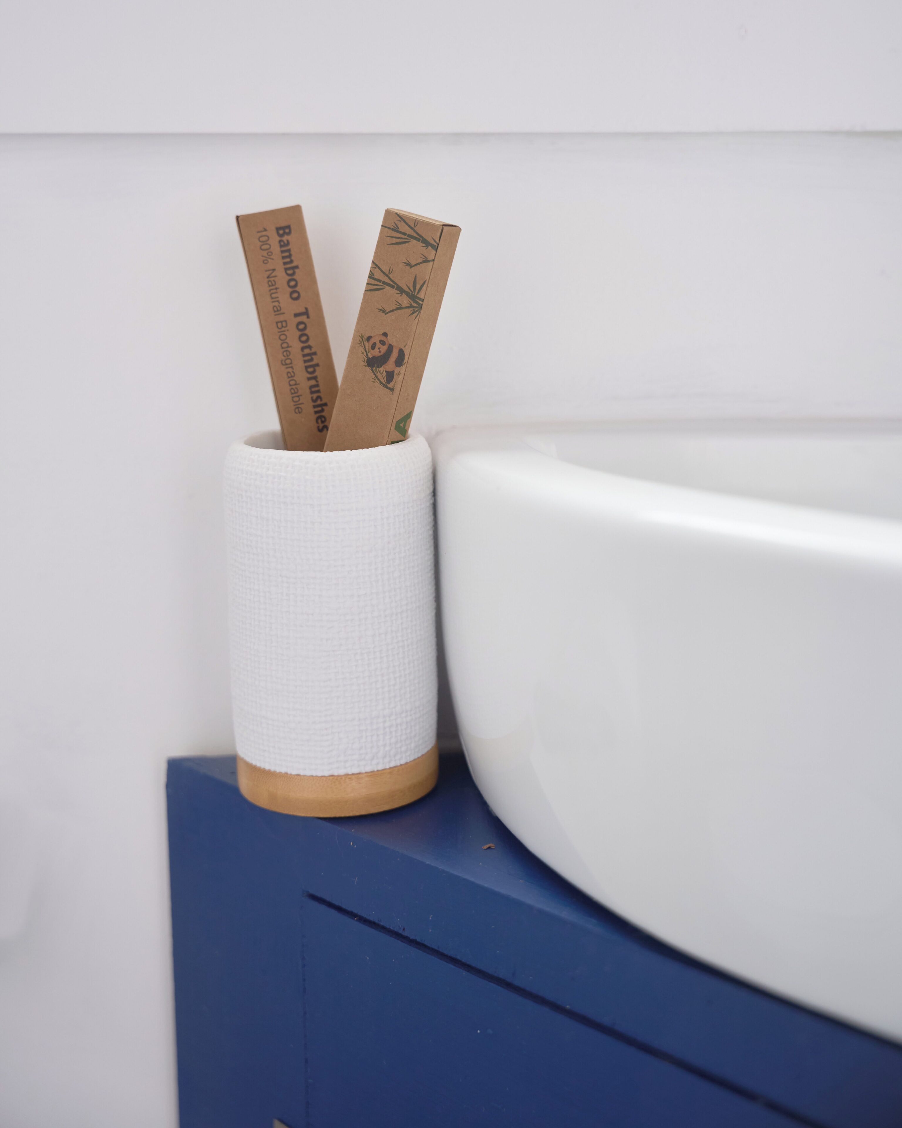 Un bany amb vàter blanc, un armari blau i un suport per al raspall de dents de bambú.