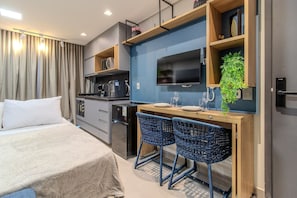 Habitación de hotel moderna con cama, kitchenette y dos sillas de mimbre azules.