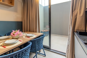 Un comedor con una mesa dispuesta para cuatro personas, sillas de mimbre azul, un cuenco con flores rosadas y una puerta corrediza de vidrio que da a un espacio al aire libre.