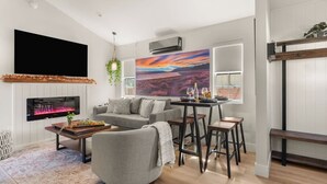 A modern living room with a fireplace, a sofa, a coffee table, and a dining area with stools. - Harvest Moon, EV charger, Hot Tub, Fire Pit (Big Bear)