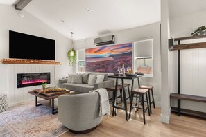 Ein modernes Wohnzimmer mit Kamin, einer Couch, einem Couchtisch und einem Essbereich mit Hockstühlen.