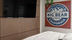 A bedroom with a bed, a mounted TV, a wall-mounted sign, and a hanging plant. - Harvest Moon, EV charger, Hot Tub, Fire Pit (Big Bear)