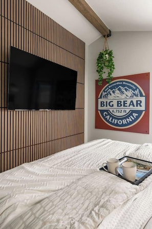 Ein Schlafzimmer mit Bett, einem an der Wand montierten Fernseher, einem Wandzeichen und einer hängenden Pflanze.