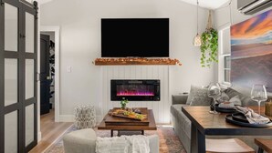 A modern living room with a fireplace, a flat-screen TV, a dining area with a table and chairs, and a sofa. - Harvest Moon, EV charger, Hot Tub, Fire Pit (Big Bear)