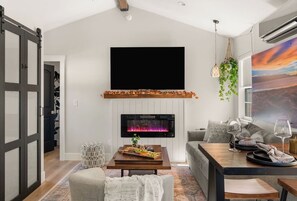Ein modernes Wohnzimmer mit Kamin, Flachbildfernseher, Essbereich mit Tisch und Stühlen sowie einer Couch.