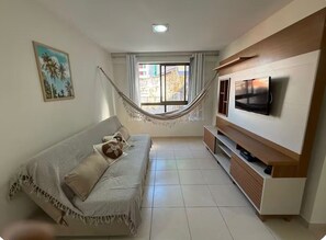 Ein Wohnzimmer mit einer Couch, einer Hängematte, einem Fernseher und einem Fenster mit Vorhängen.