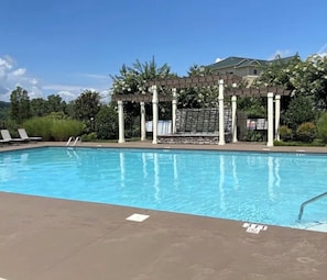 A swimming pool with a pergola structure, lounge chairs, and a building in the background.