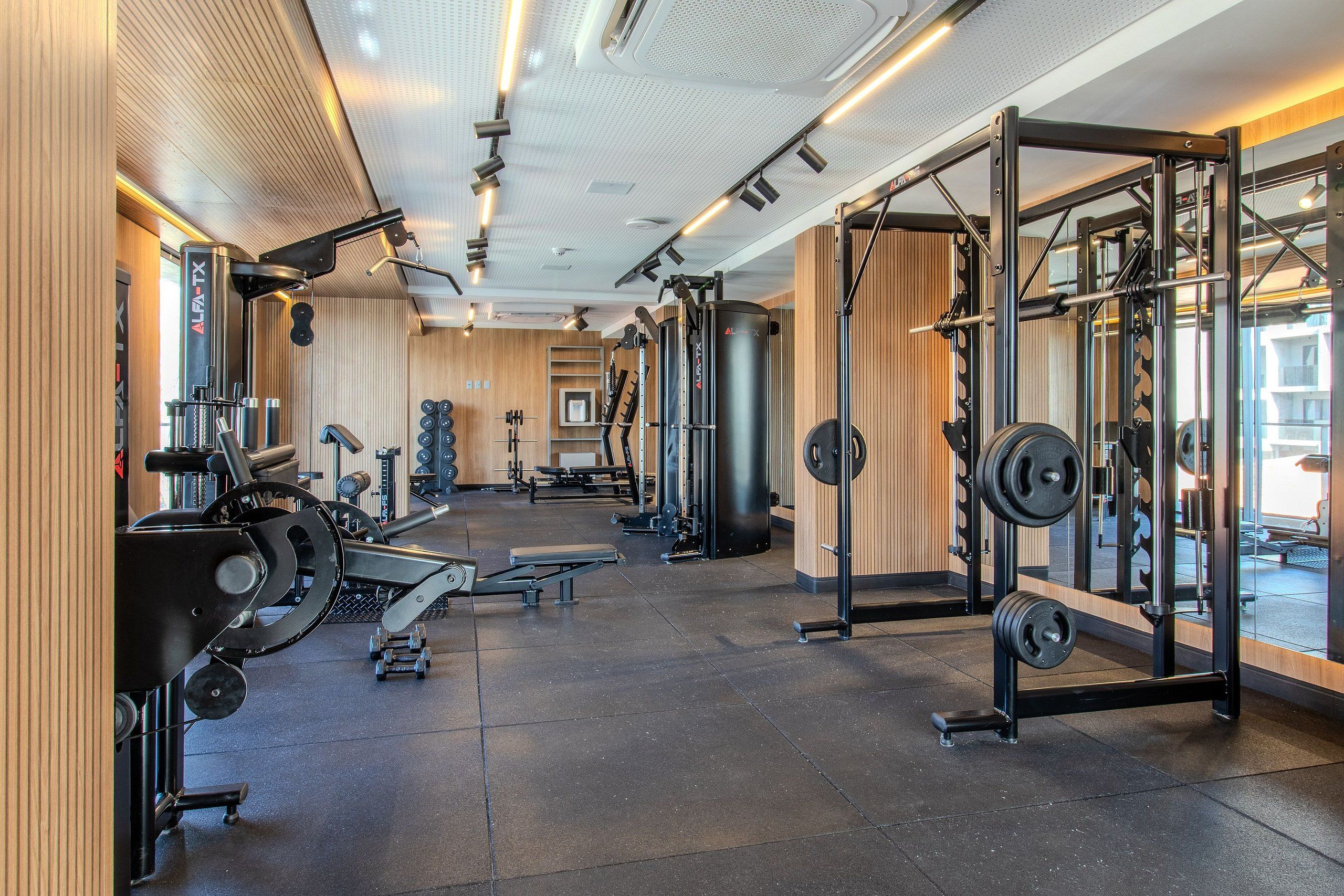 A gym with weightlifting equipment, mirrors, and a wooden wall.