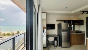 Un balcón con vista a la playa, una kitchenette con refrigerador, televisor y una silla.