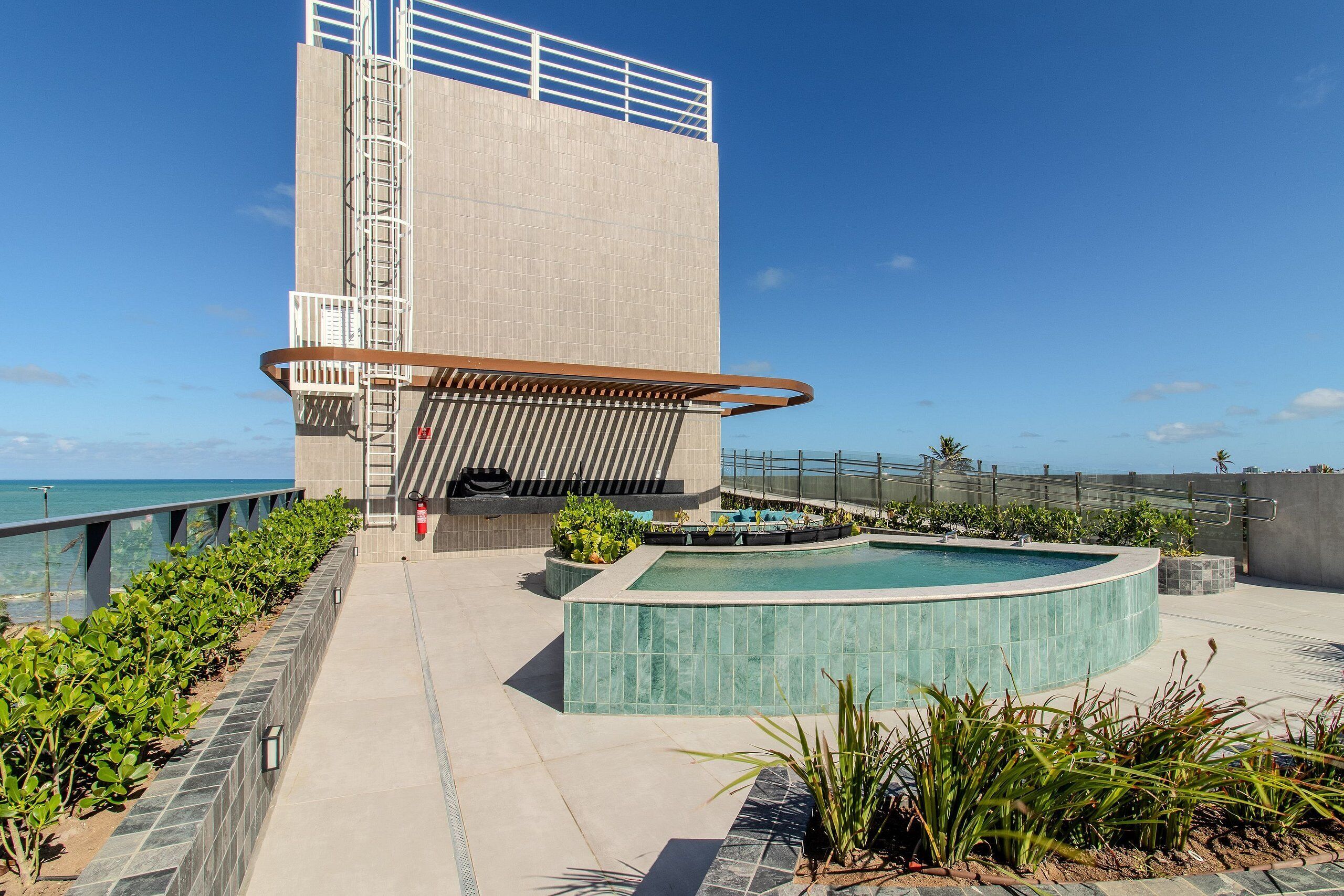 Um edifício moderno com piscina, escadaria de metal e vista para o oceano.