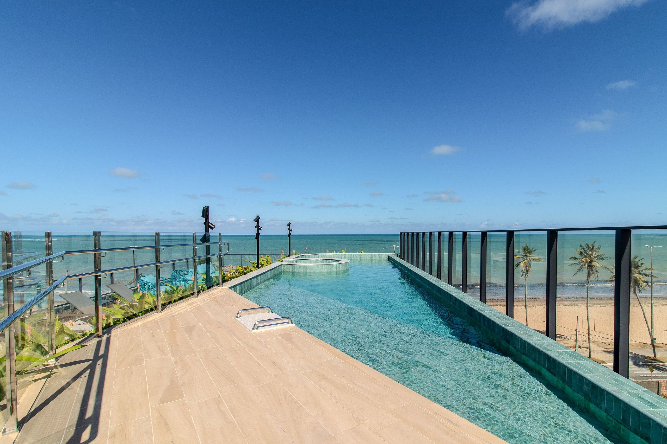 A pool with clear water, a wooden deck, and a view of the beach and ocean.