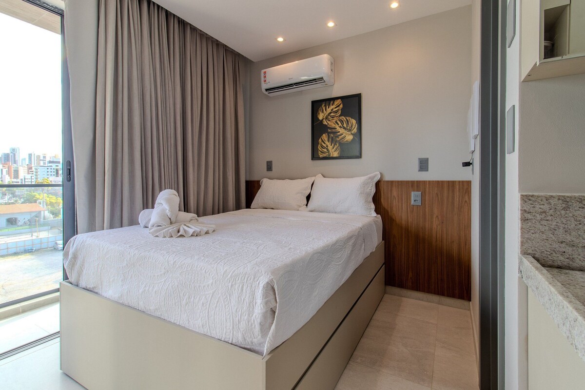 Una habitación de hotel moderna con una cama grande, un equipo de aire acondicionado, vistas a la ciudad y una obra de arte enmarcada en la pared.