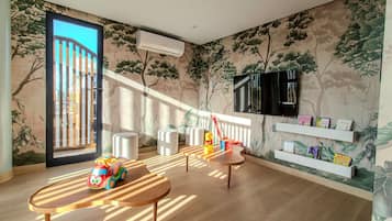 A room with a large window, a wall-mounted TV, and a shelf with children's books.