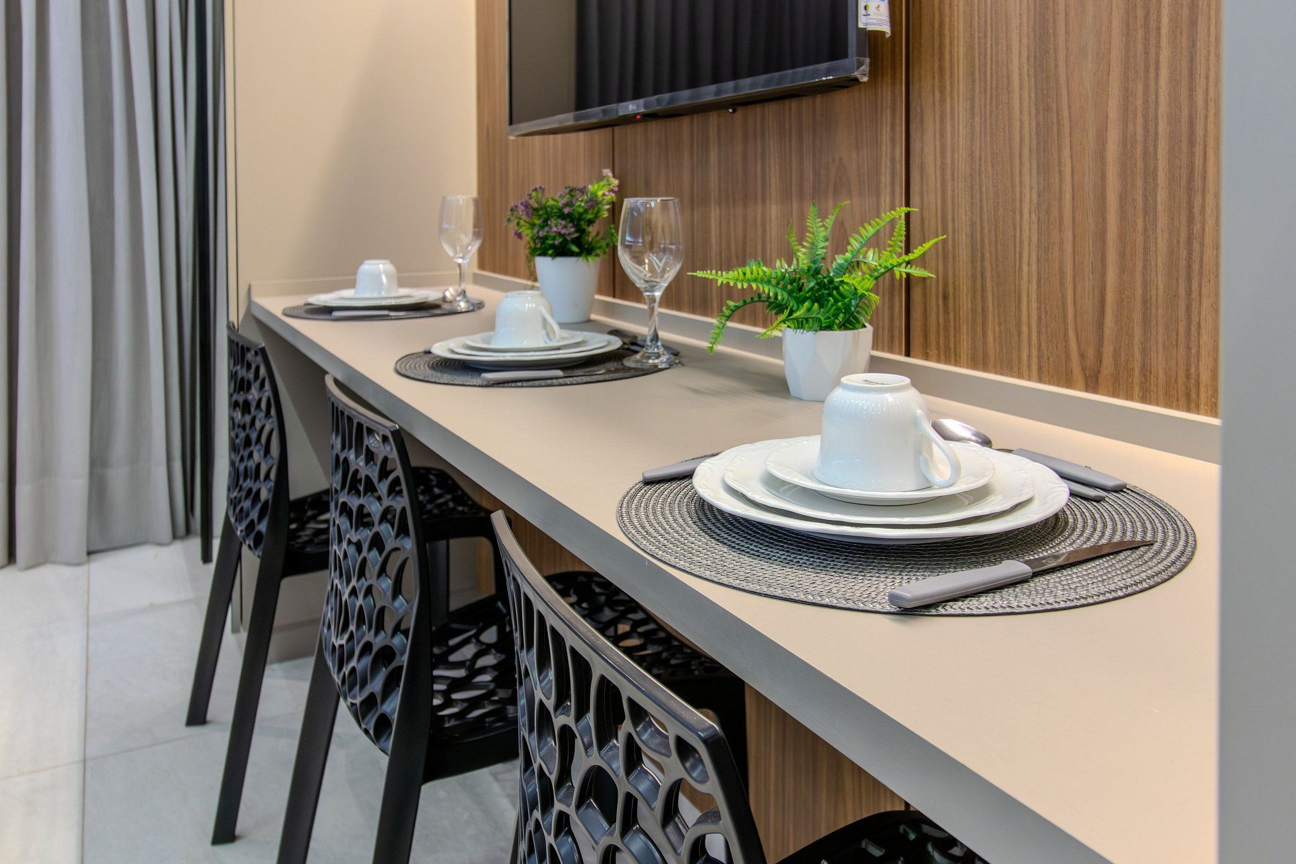 A dining table set with plates, glasses, and cutlery, with chairs and a potted plant on a modern table.