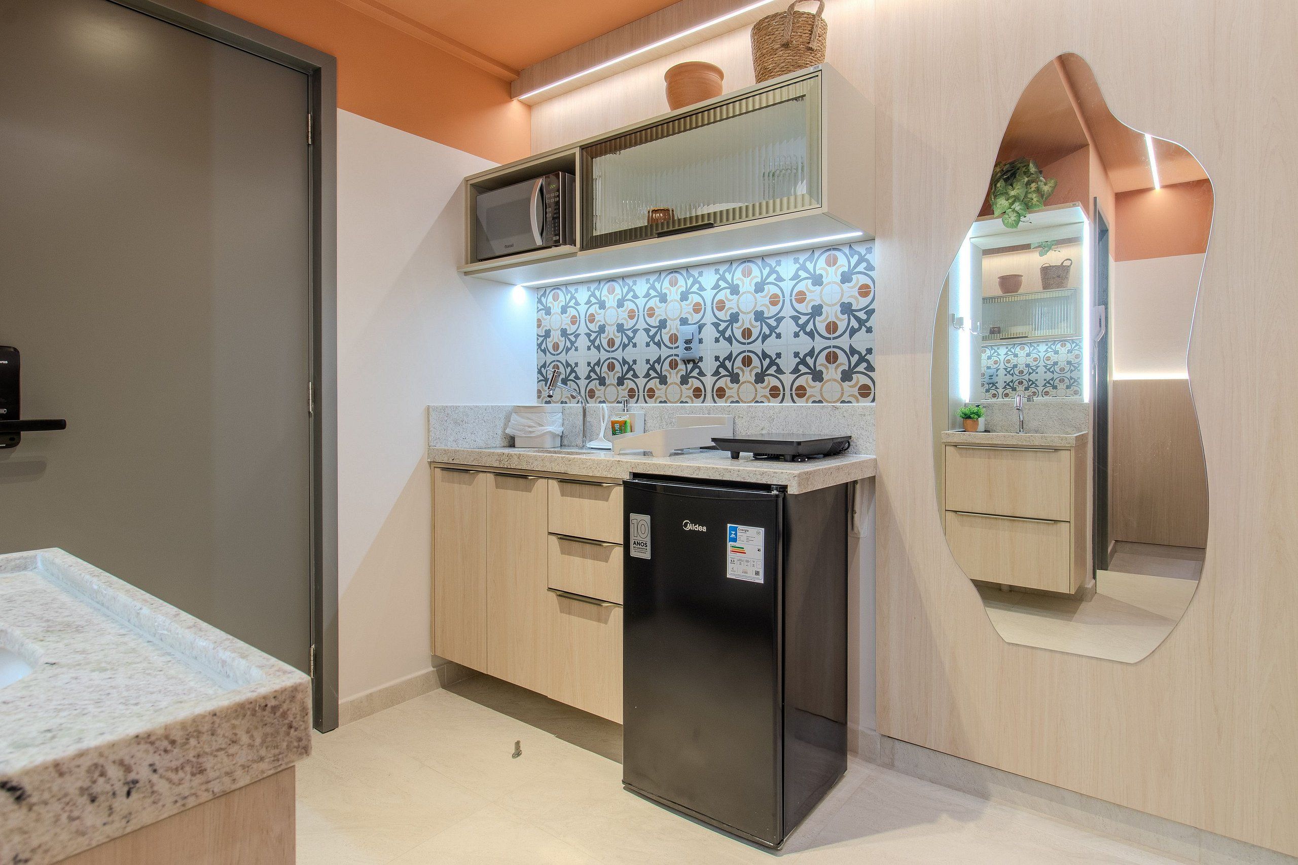 A modern kitchen with a built-in refrigerator, microwave, and a unique curved mirror design.
