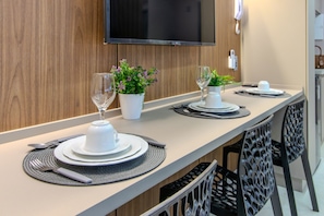 Een eethoek met een lange tafel, witte borden, bestek en potplanten.