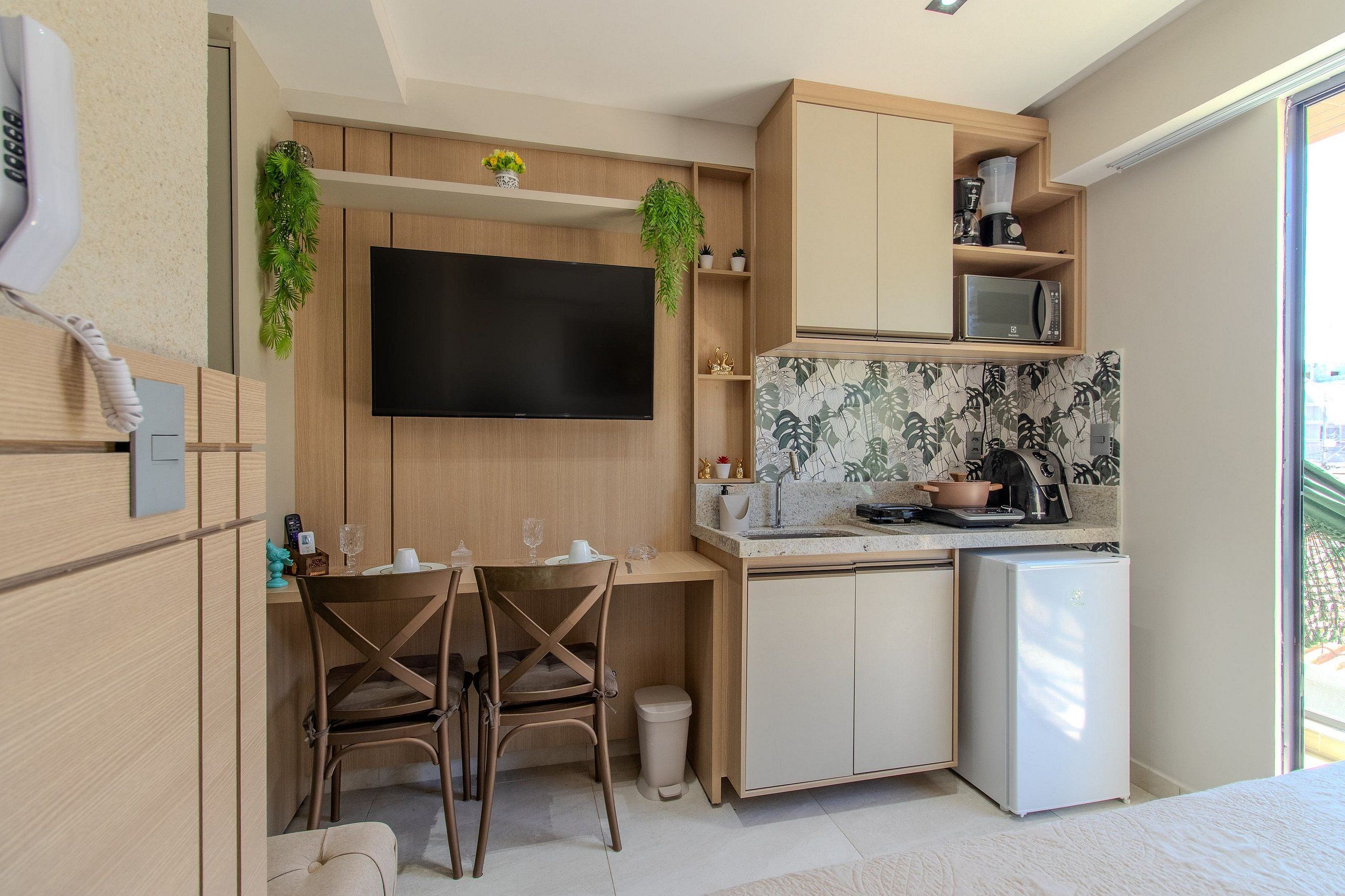 Cocina compacta equipada con microondas, refrigerador y televisor de pantalla plana montado en la pared.