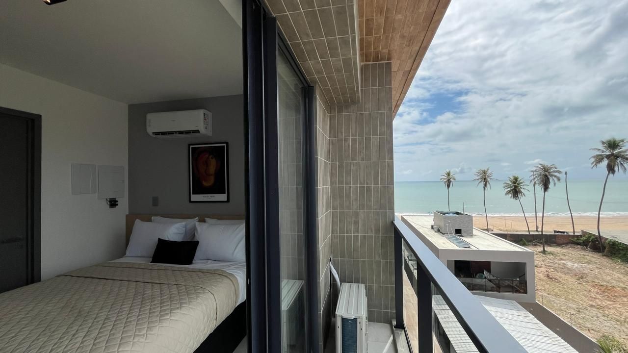 Quarto com cama, ar condicionado, quadro emoldurado e vista para a praia.