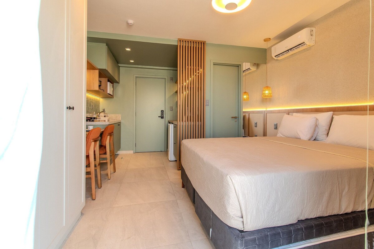 Una habitación de hotel con cama, escritorio con sillas, kitchenette y aire acondicionado.