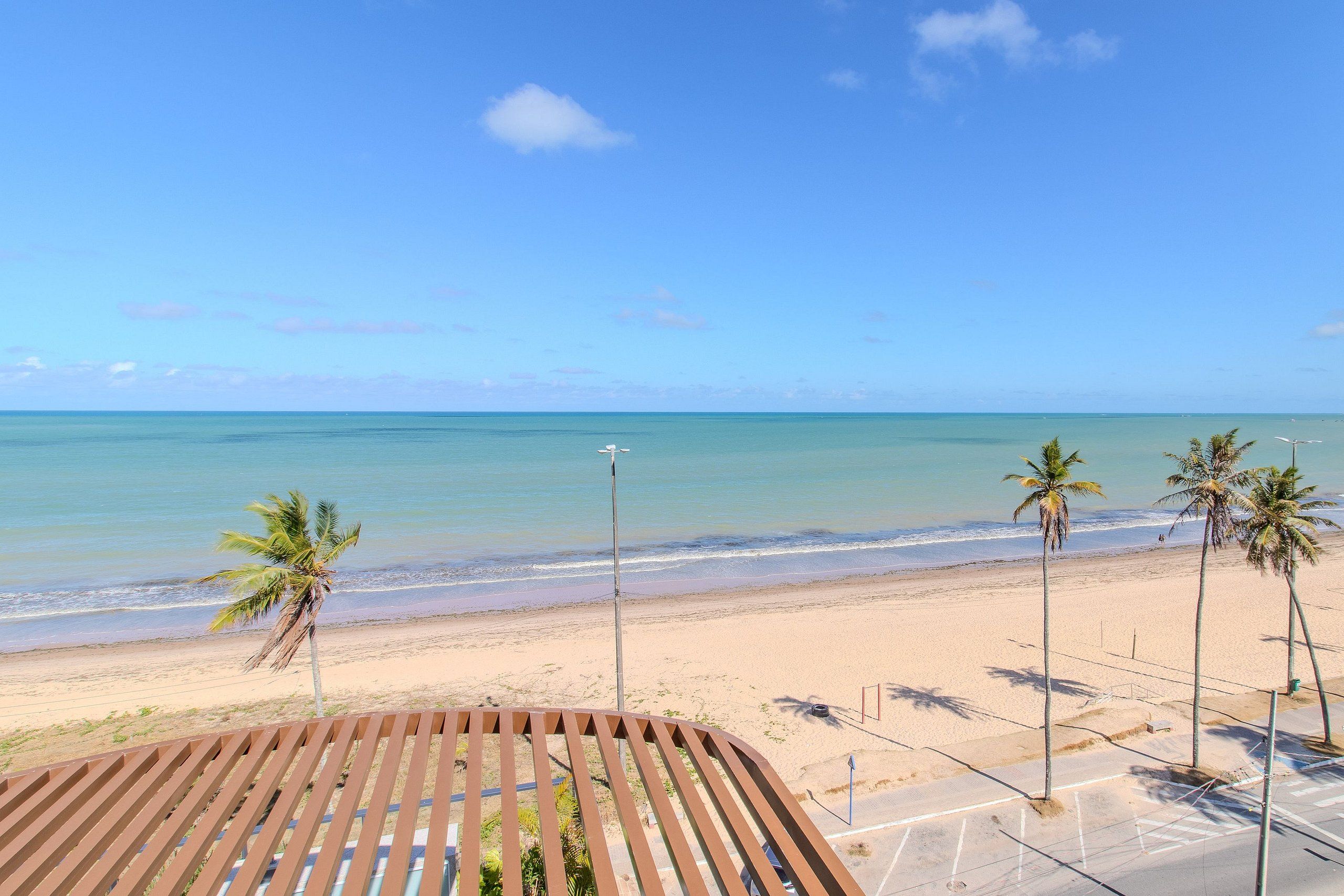 A beach view with palm trees, a wooden deck, and a parking area.