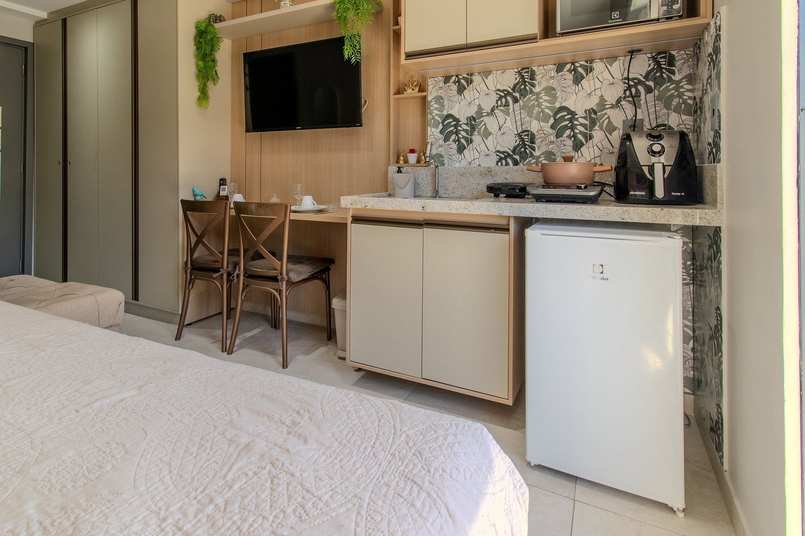 Una habitación pequeña y funcional con cama, escritorio y kitchenette.